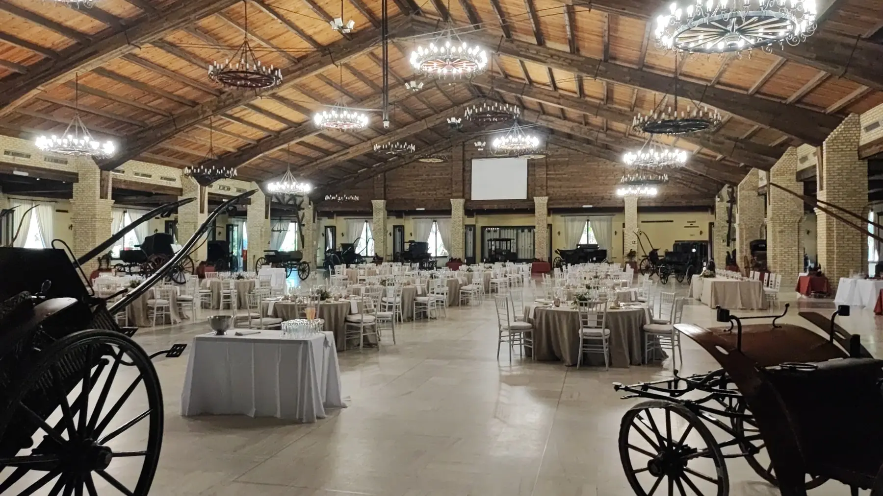 Mesas de banquete montadas en un gran salón, entre carruajes y lámparas